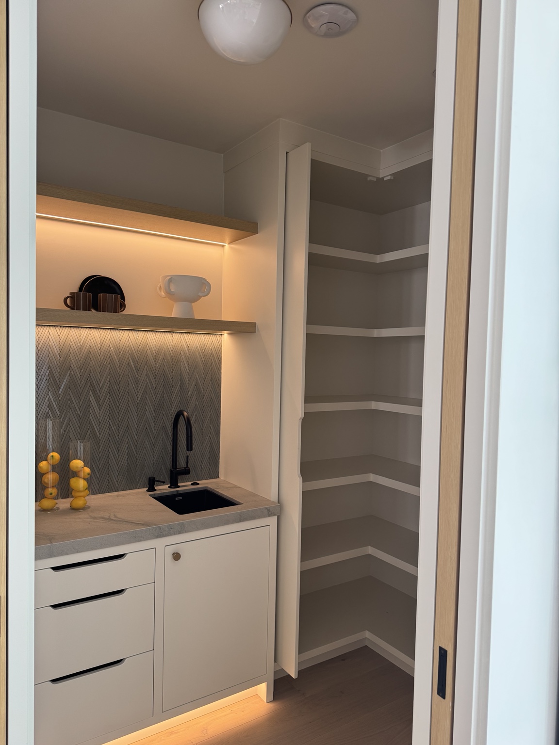 Small pantry with concealed shelf and toe-kick linear lighting